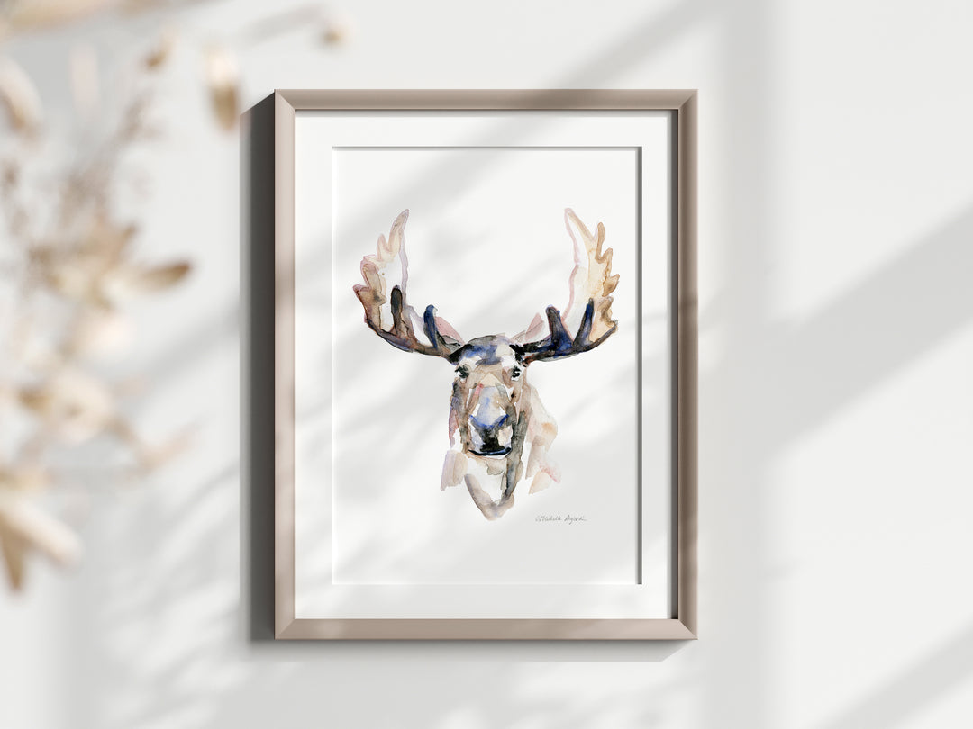 Framed artwork of a moose head on a white wall with decorative elements.