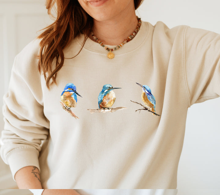 Person wearing a beige sweatshirt with kingfisher bird designs.