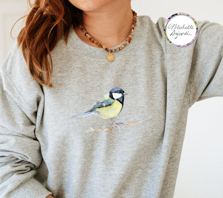 Person wearing a gray sweatshirt with a great tit bird design, branded 'Michelle Dujardin'.