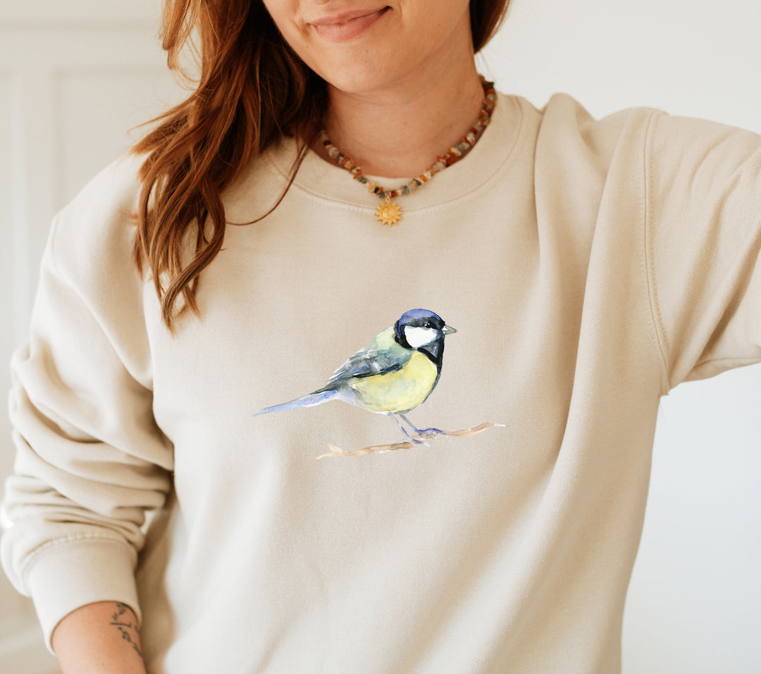 Person wearing a beige sweatshirt with a great tit bird design on a plain background