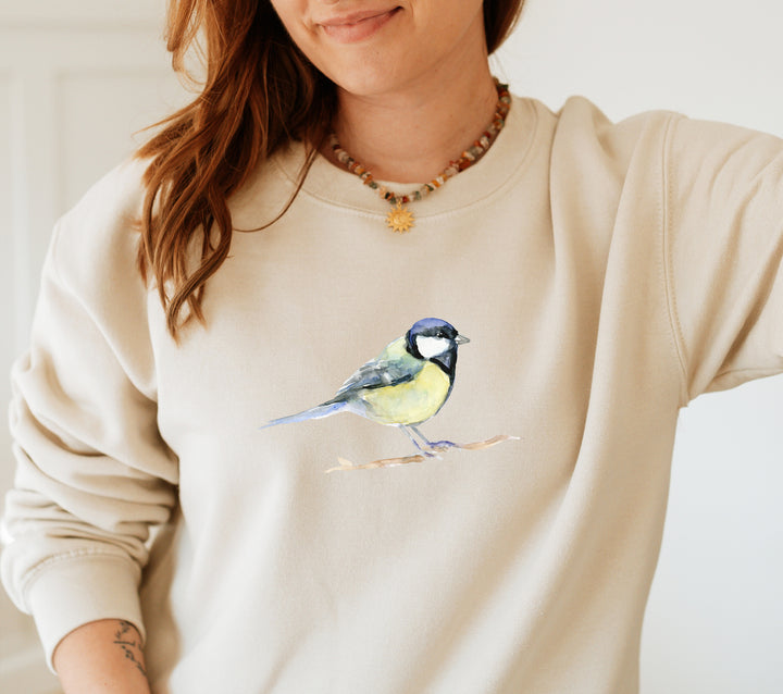Person wearing a beige sweatshirt with a great tit bird design on a plain background