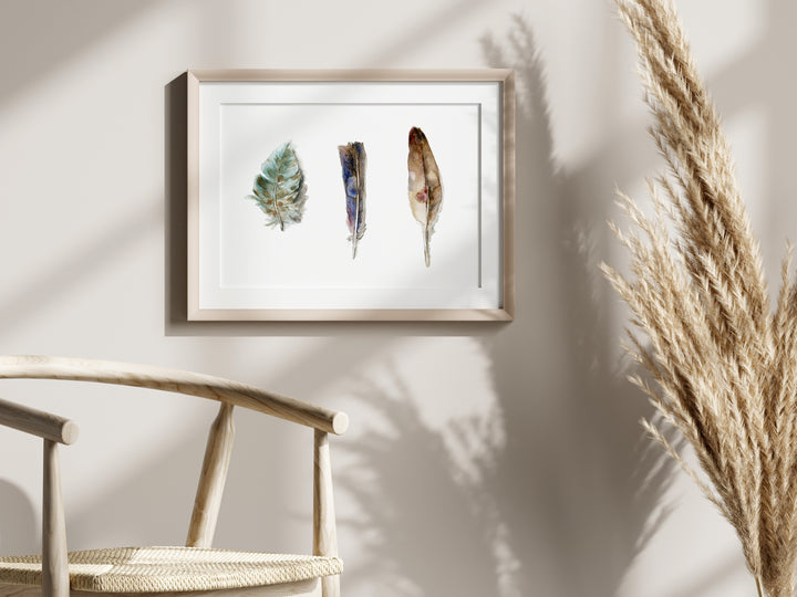 Framed artwork of feathers on a wall with a chair and dried plants in the foreground
