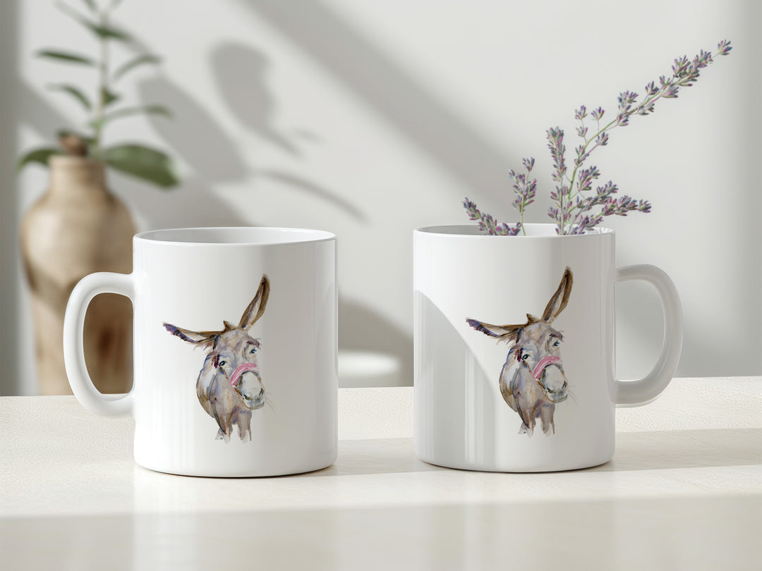 Two white mugs with donkey illustrations on a light surface with a plant in the background.