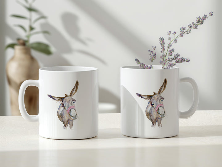 Two white mugs with donkey illustrations on a light surface with a plant in the background.