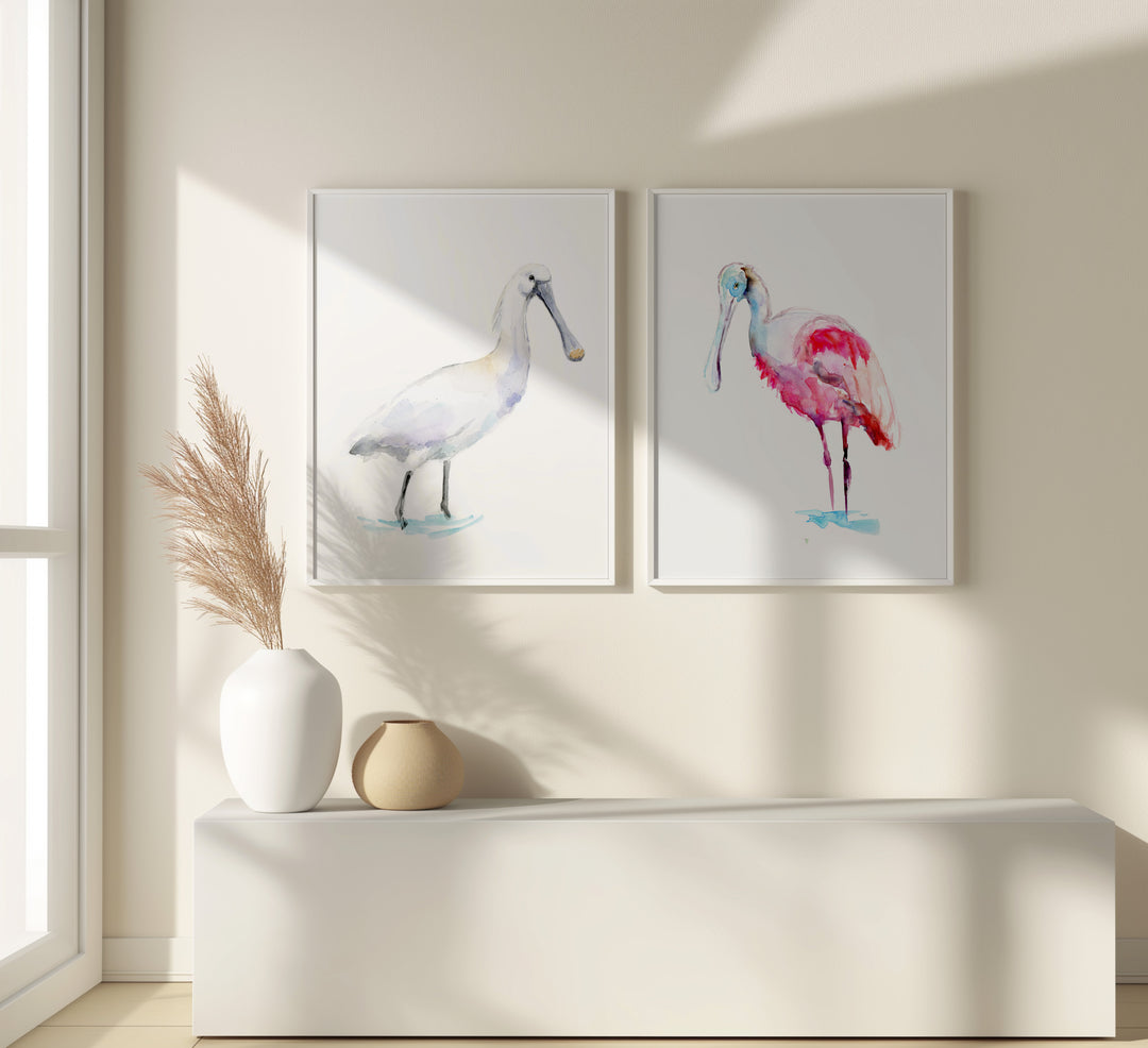 Two framed paintings of spoonbill birds on a wall with decorative vases below.