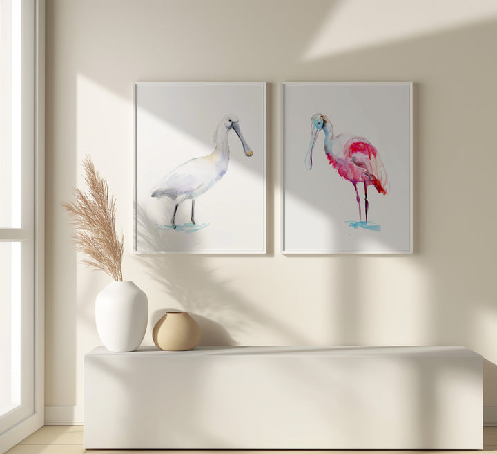 Two framed paintings of spoonbill birds on a wall with decorative vases below.