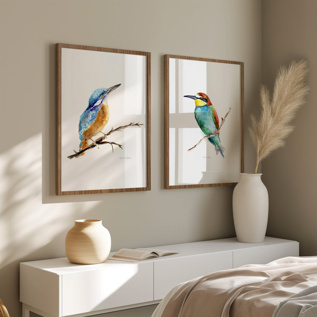 Two framed bird prints on a wall above a white cabinet with decorative vases.