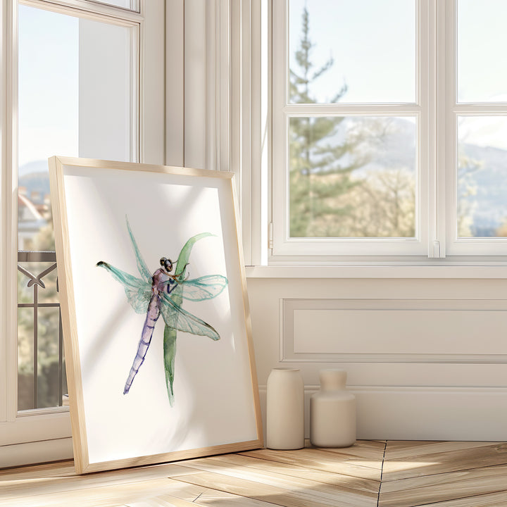 Framed artwork of a dragonfly on a white wall in a room with large windows.