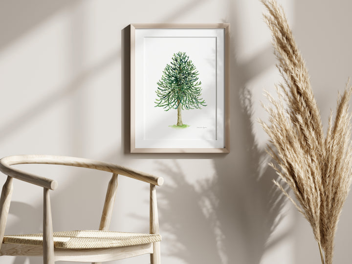 Framed artwork of a green tree on a wall with a chair and dried plants in the foreground.