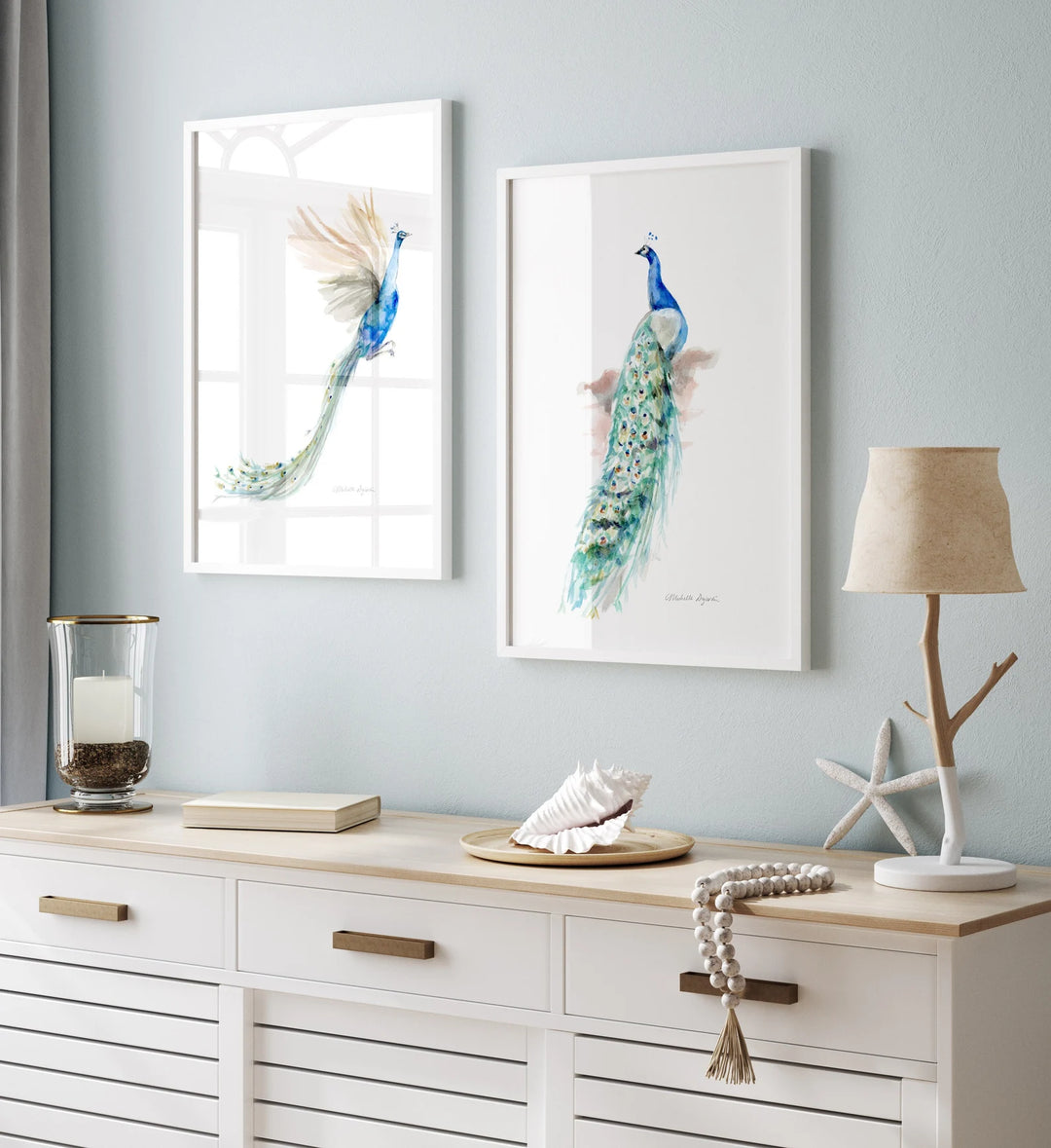 Two framed peacock artworks on a wall above a wooden console table with decorative items.