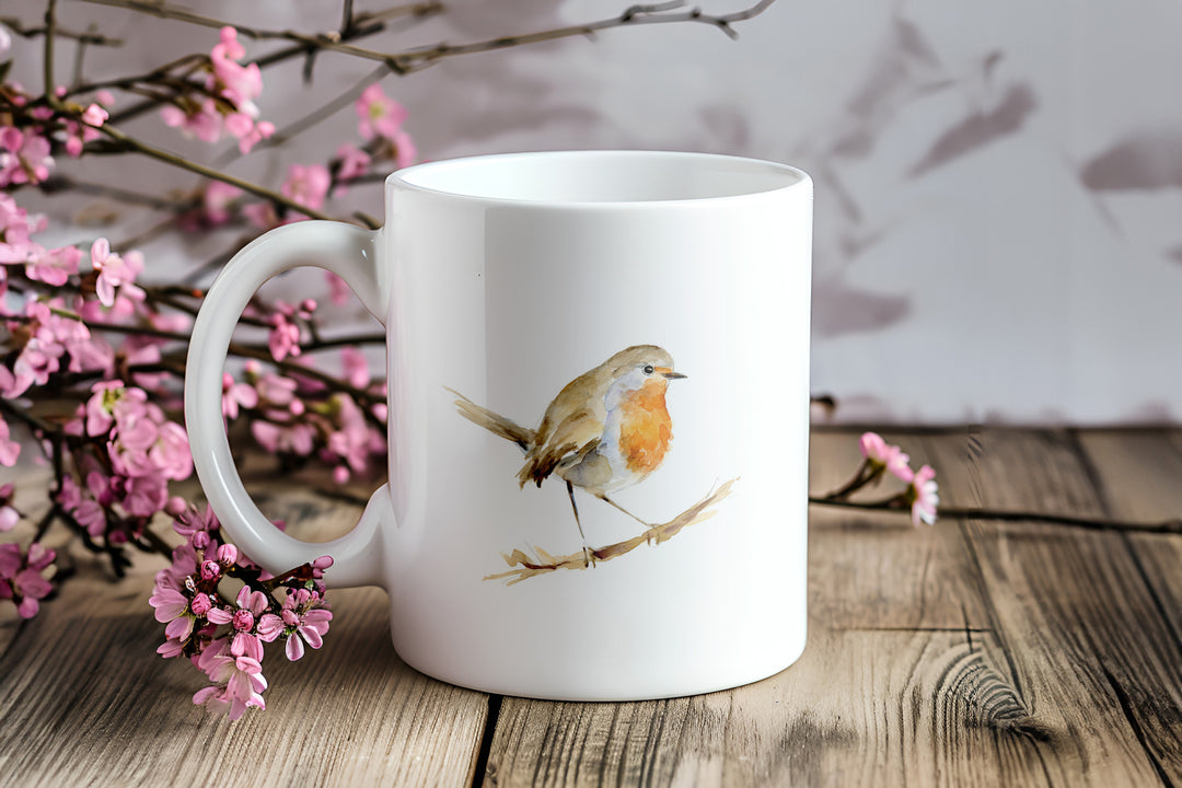 White mug with a robin design on a wooden surface with pink flowers.