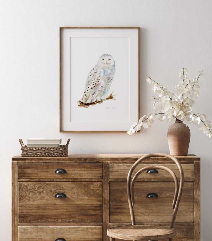 Wooden dresser with a framed snowy owl print and decorative items on a light gray wall.